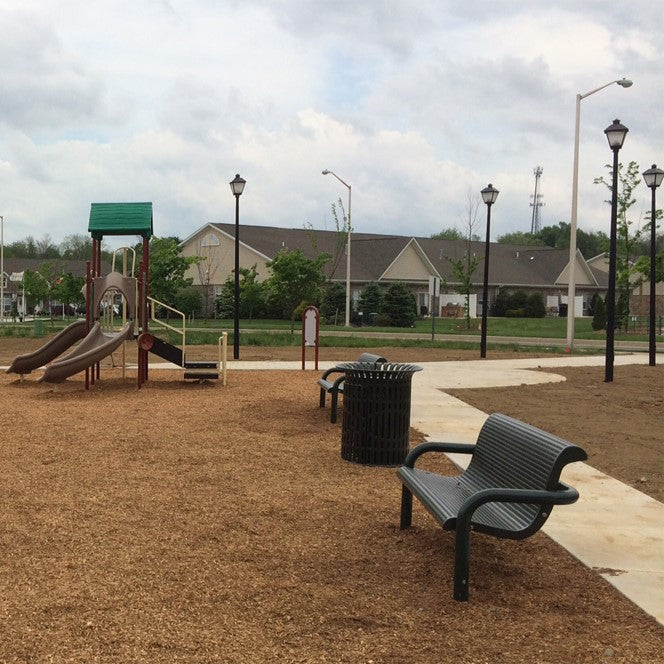 Playground with slides and a bench in an open area with buildings in the background