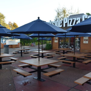 Outdoor seating area with tables, benches, and blue umbrellas in front of a pizza restaurant.
