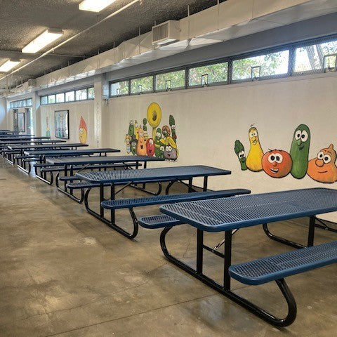 Row of blue picnic tables with colorful vegetable murals on a wall in an indoor setting.