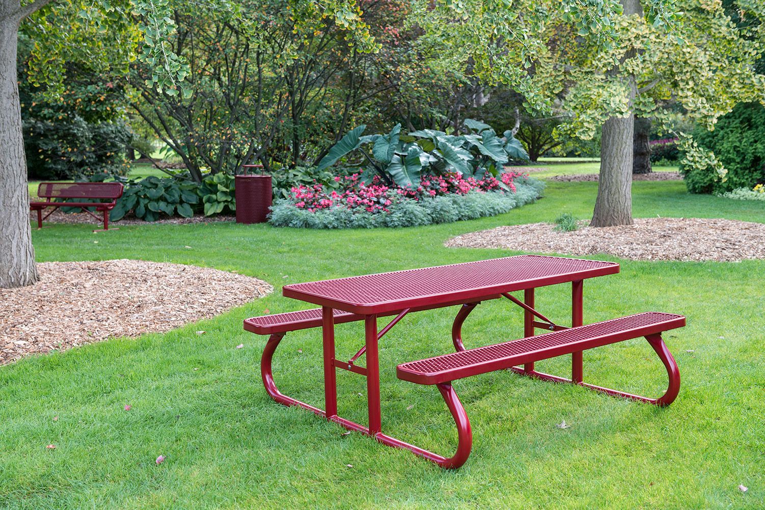 Red picnic table in a park setting with green grass and trees.